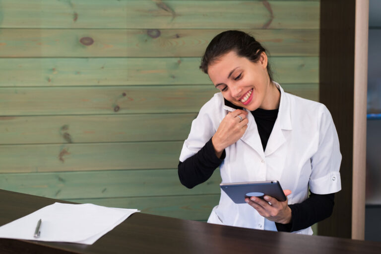 Receptionist dell'area wellness dell'hotel guarda un tablet mentre telefona sorridendo.